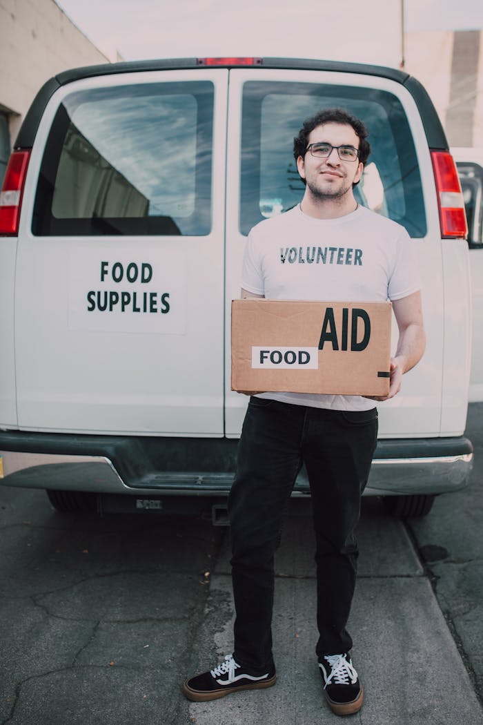 services-02 Volunteer standing in front of food supplies van with aid box, supporting community.
