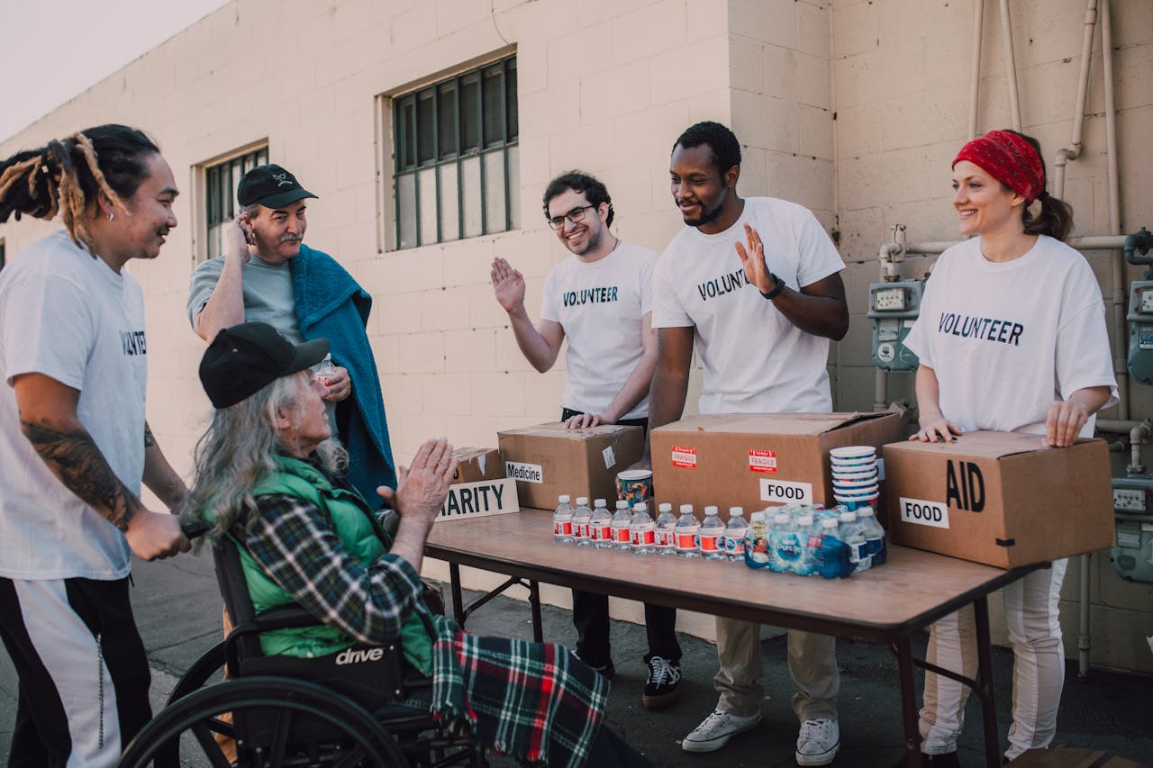 heros-img Group of volunteers providing food and aid to a person in wheelchair outdoors.