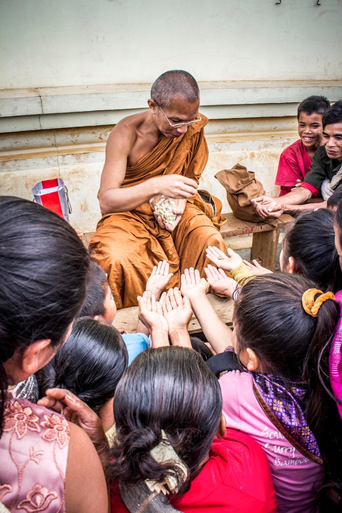 who-we-are An Asian monk in orange robes distributes food to eager children outdoors.